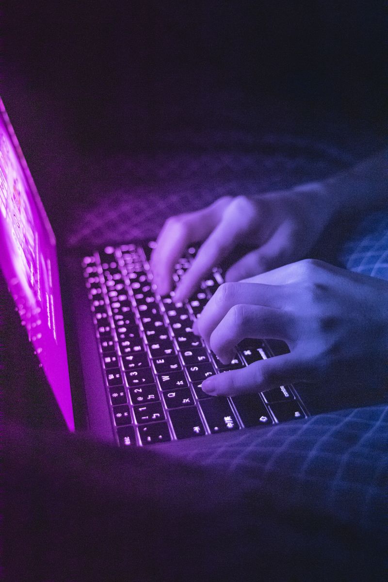 Hands typing on a laptop keyboard in blue and violet light
